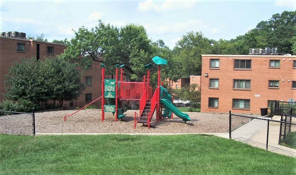 A playground with a red and green slide in front of a brick building.